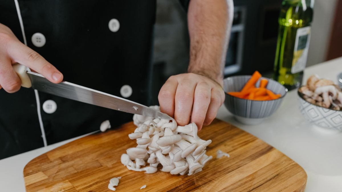 Close-up of a chef cutting white mushrooms on a wooden board in a kitchen setting.